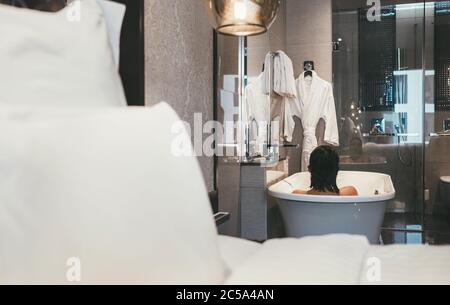 Femme voyageur prenant un bain dans la salle de bains de l'hôtel 5 étoiles de haute qualité. Elle se coutait dans le tube de bain blanc profond, se détendant et appréciant l'eau chaude. Santé an Banque D'Images