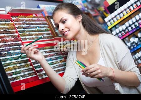 Smiling brunette girl picking différents crayons dans département artistique Banque D'Images