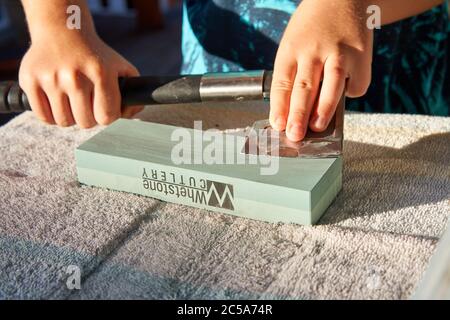 Travailler avec les mains pour affûter une hache émoussée à l'aide d'une pierre à affûter sur la table. Banque D'Images