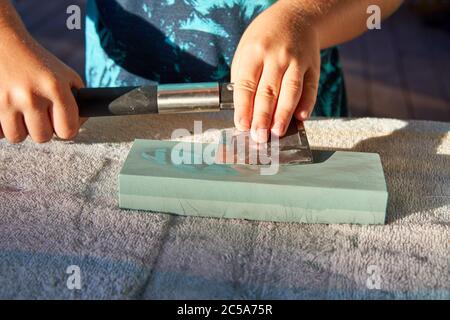 Travailler avec les mains pour affûter une hache émoussée à l'aide d'une pierre à affûter sur la table. Banque D'Images