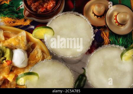 Vue panoramique sur trois cocktails margarita entourés de nachos, de frites et de salsa sur une nappe mexicaine lumineuse. Format horizontal. Parfait pour ci Banque D'Images