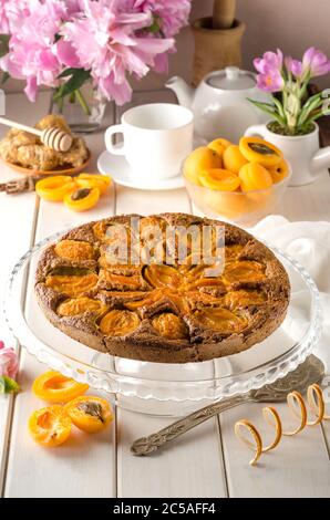 Tarte ronde à l'abricot sur fond de bois blanc avec un bouquet de péonies. Banque D'Images