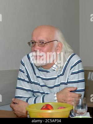 Gros plan portrait en demi-longueur d'un homme âgé chauve aux cheveux longs gris et à la barbe dans un chandail rayé qui est assis à la table. Banque D'Images