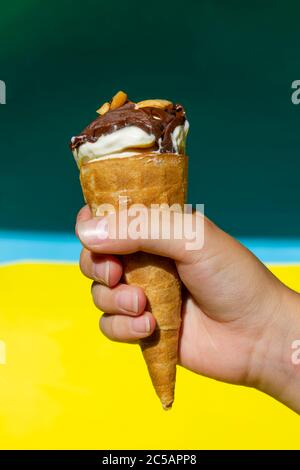 Garçon tient la glace dans un cône. Crème glacée dans un corne sur fond jaune-bleu. Arachide. copyspace Banque D'Images