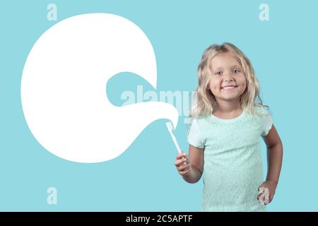 Une jeune fille blonde avec un sourire montre comment vous brosser les dents. Concept sur le sujet des soins dentaires. Publicité de clinique dentaire. Sur fond bleu menthe. Banque D'Images