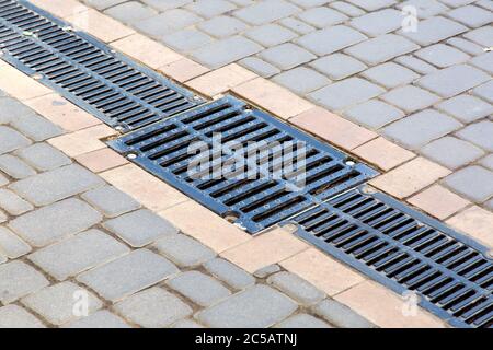 Réseau d'un système de revêtement de drainage avec grille à trappe sur un chemin en carreaux de pierre carrée, gros plan d'un système de drainage d'eau de pluie. Banque D'Images