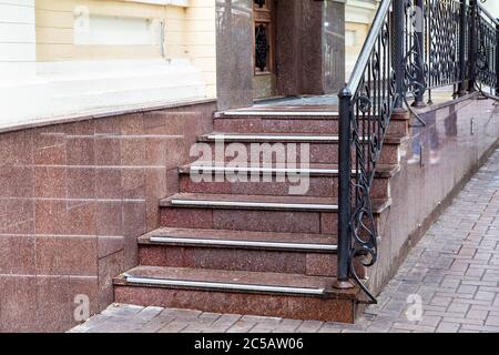 escalier en marbre avec une montée à la porte d'entrée avec bandes antidérapantes en caoutchouc et mains courantes forgées noires, seuil avec entrée de marches rapprochée. Banque D'Images