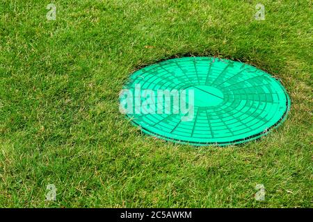 Trappe verte d'un système d'égout dans un défrichement avec de l'herbe verte, fermer trou d'homme sur la prairie. Banque D'Images