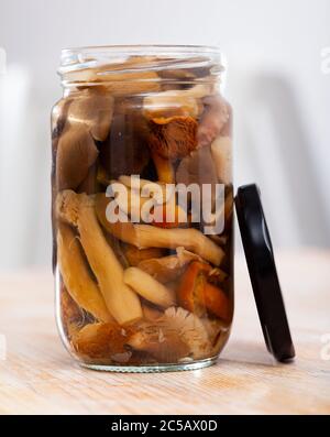 Mélanger divers champignons marinés dans un pot en verre ouvert sur une table en bois Banque D'Images