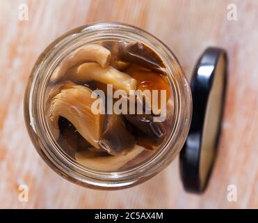 Mélanger divers champignons marinés dans un pot en verre ouvert sur une table en bois Banque D'Images