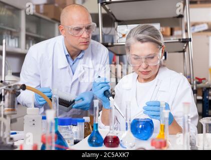 Recherche scientifique en laboratoire. Deux scientifiques mélangent des réactifs dans un tube à essai avec une pipette de laboratoire Banque D'Images