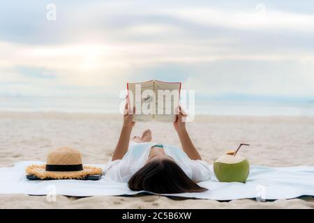 Jeune femme asiatique couché sur une mer tropicale d'été plage pour se détendre lire livre avec jus de noix de coco à côté d'elle. Été, vacances, vacances et Happy Peop Banque D'Images