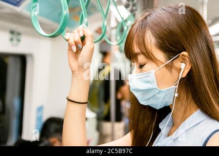 Jeune femme asiatique passager portant un masque chirurgical et écoutant de la musique par téléphone portable dans le métro Banque D'Images