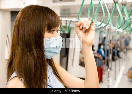 Jeune femme asiatique passager portant un masque chirurgical et écoutant de la musique par téléphone portable dans le métro Banque D'Images