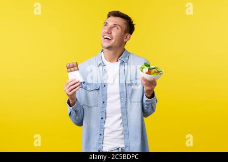 Mode de vie sain, personnes et concept alimentaire. Un homme souriant et souriant qui regarde dans le coin supérieur gauche tout en tenant un bol avec une salade et un bar à bonbons debout Banque D'Images