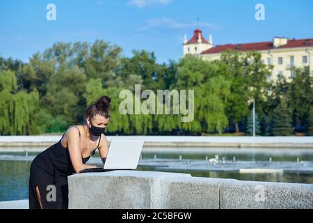belle fille dans un masque marche dans la ville, travaillant sur un ordinateur portable. tenant un ordinateur portable et écoutant de la musique. Banque D'Images