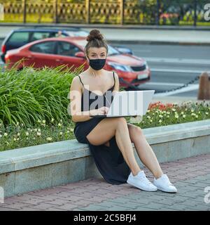 belle fille dans un masque marche dans la ville, travaillant sur un ordinateur portable. tenant un ordinateur portable et écoutant de la musique. Banque D'Images