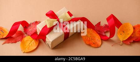 Cadeau de vacances créatif d'automne. Boîte cadeau en papier fait main avec noeud en satin, feuilles séchées sur fond beige. Jour de Thanksgiving, arrière-plan d'automne. Banque D'Images