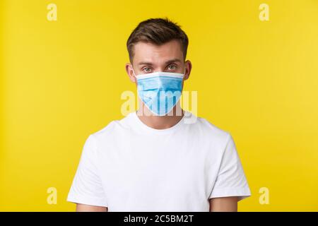 Concept de distanciation sociale, covid-19 et les émotions des gens. Homme sérieux dans le masque médical et le t-shirt de base regardant la caméra concernée, auto-isolation Banque D'Images