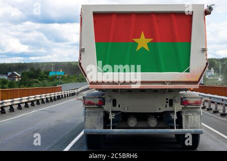 Un gros camion avec le drapeau national du Burkina Faso se déplaçant sur la route, dans le fond du village et du paysage forestier. Concept d'expo Banque D'Images