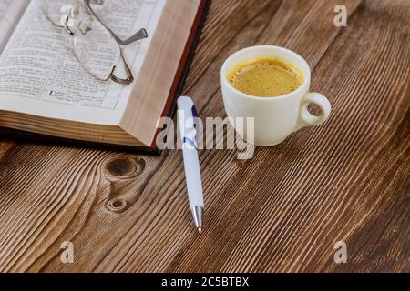 Los Angeles CA US 01 JUILLET 2020: Étude du matin personnelle avec la Sainte Bible ouverte avec tasse de café noire sur stylo avec lunettes sur fond de bois Banque D'Images