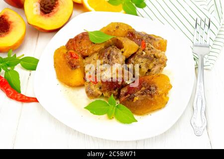 Dinde à la sauce aux pêches, piment frais et sauce à l'orange, feuilles de basilic dans une assiette, serviette, fruits sur fond de bois clair Banque D'Images