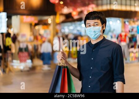 Un jeune homme asiatique qui fait ses courses avec un sac au centre commercial et porte un masque médical pour prévenir la pandémie du coronavirus (Covid-19). Nouveaux concepts normaux Banque D'Images