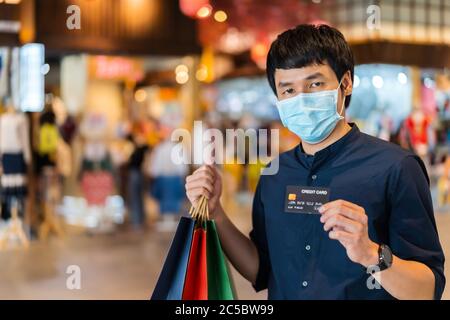 Jeune asiatique portant un masque médical et tenant une carte de crédit au centre commercial pour prévenir la pandémie du coronavirus (Covid-19). Nouveau concep normal Banque D'Images