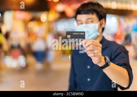 Carte de crédit avec un jeune homme asiatique portant un masque médical au centre commercial pour la prévention de la pandémie du coronavirus (Covid-19). Nouveaux concepts normaux Banque D'Images