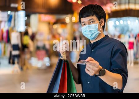 Jeune asiatique portant un masque médical et tenant une carte de crédit au centre commercial pour prévenir la pandémie du coronavirus (Covid-19). Nouveau concep normal Banque D'Images