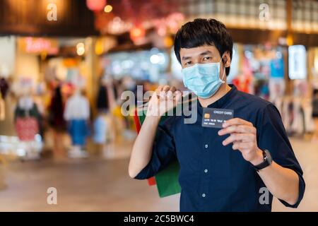 Jeune asiatique portant un masque médical et tenant une carte de crédit au centre commercial pour prévenir la pandémie du coronavirus (Covid-19). Nouveau concep normal Banque D'Images