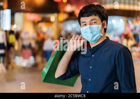 Un jeune homme asiatique qui fait ses courses avec un sac au centre commercial et porte un masque médical pour prévenir la pandémie du coronavirus (Covid-19). Nouveaux concepts normaux Banque D'Images