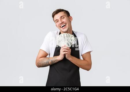 Concept de petite entreprise de vente au détail, de paiements et d'employés. Un barista souriant et gai dans un tablier noir, un vendeur qui apprécie le paiement, enserre l'argent et Banque D'Images