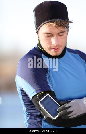 Musique d'entraînement sur l'application smartphone : homme coureur écoutant de la musique réglage des paramètres sur le brassard pour smartphone. Modèle de fitness masculin travaillant en extérieur à la fin de l'automne ou en hiver, dans une tenue sportive. Banque D'Images