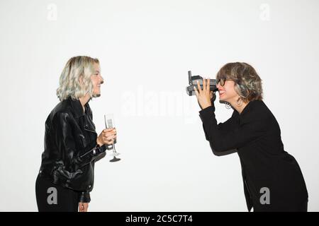 Belle fille souriante en blouson noir heureux de prendre des photos sur polarid appareil photo de jolie fille avec un verre de champagne à la main sur fond blanc Banque D'Images