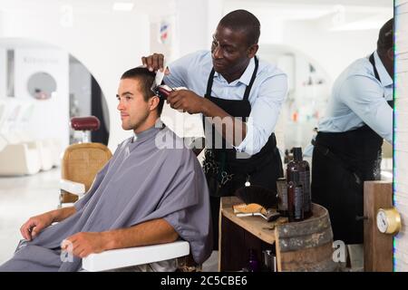 Jeune homme obtenir même avec electric clipper par des professionnels de coiffure africaine à salon Banque D'Images