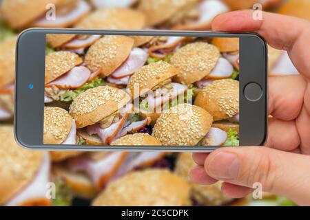 Hors-d'œuvre froids sur le plateau hamburger avec du bacon et des herbes dans plusieurs rangées. Sandwichs sur l'écran du smartphone. Banque D'Images