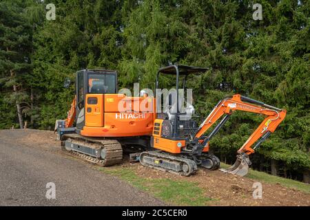 Deux excavatrices sur chenilles Hitachi stationnées sur une route de haute montagne nouvellement construite sur un fond de forêt de conifères vertes, Alpes, Italie. Banque D'Images