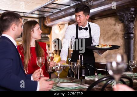 L'homme est chef de l'ordre apporte au couple qui avons le dîner et boire du vin dans un restaurant. Banque D'Images