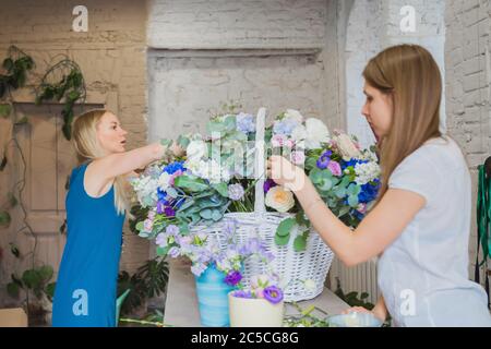 Deux artistes fleuristes professionnels, fleuristes en train de réaliser un grand panier floral avec des fleurs à l'atelier, fleuriste. Fleuriste, fait main, mariage Banque D'Images