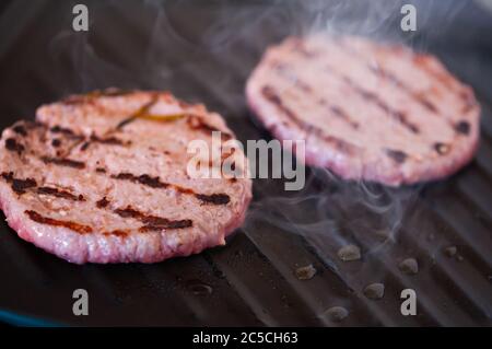 Concept de cuisson, de barbecue et de restauration rapide : gros plan de côtelettes de viande de hamburger rôtisant sur un gril plus brazier Banque D'Images