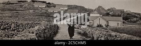 Vue du début des années 1920 d'une femme en robe traditionnelle qui descend une boreen entre des murs de pierre sèche sur Inishmaan, une des îles Aran au large du comté de Galway sur la côte ouest de l'Irlande. Initialement photographié par A. W. Cutler (1875-1935) pour 'Ireland: The Rock Wharce I was hewn', un reportage du magazine National Geographic de mars 1927. Banque D'Images