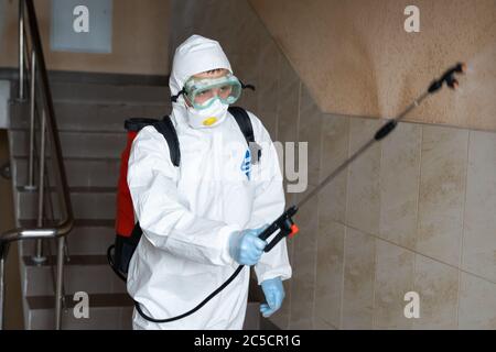 UKRAINE, KIEV - 20 mai 2020: L'homme dans un costume et un masque de protection blanc assainit les surfaces intérieures à l'intérieur des bâtiments pendant l'épidémie de coronavirus Banque D'Images