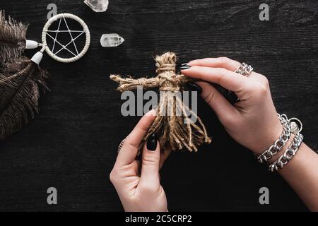 vue de dessus de la femme tenant voodoo poupée dans les mains près de pentagram et cristaux sur noir Banque D'Images