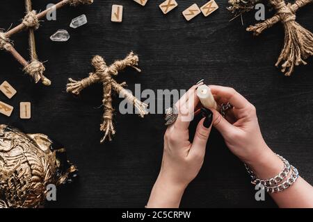 vue de dessus de la femme tenant une bougie en feu près des poupées voodoo, runes, cristaux et crâne sur noir Banque D'Images