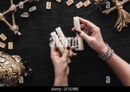 vue de dessus de la femme tenant des bougies près du crâne, runes, poupée voodoo et cristaux sur noir Banque D'Images