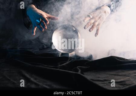 Vue rognée d'une sorcière effectuant un rituel avec boule de cristal sur fond sombre Banque D'Images