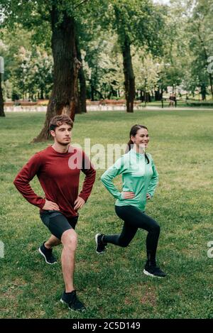 Souriant sportswoman faisant des fentes près de l'ami dans le parc Banque D'Images