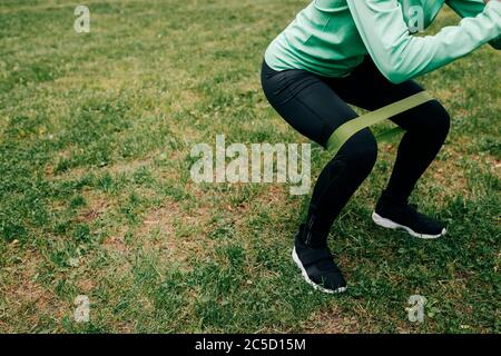 Vue rognée de sportswoman faisant du squat avec bande de résistance sur l'herbe dans le parc Banque D'Images