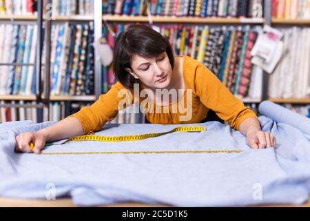 Vendeuse compétente a ordonné de mesure pour la coupe de tissu textile en boutique, la préparation pour la vente Banque D'Images